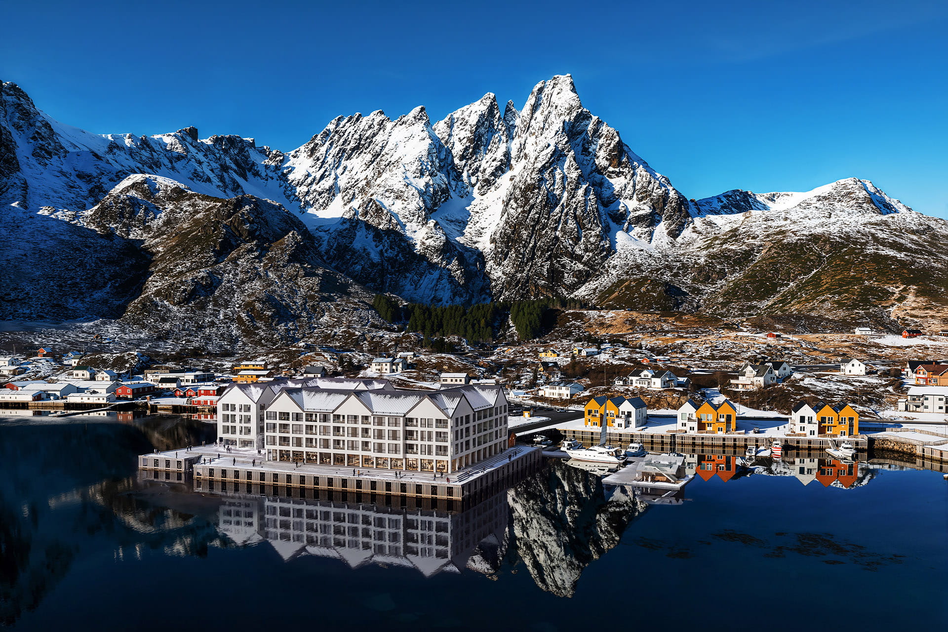 Winter waterfront view of Reineholmen Resort reflected in Ballstad harbour beneath snow-covered mountains